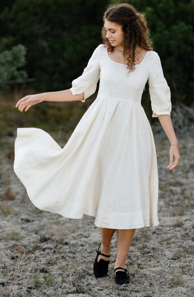 A woman wearing a milky white Son de Flor wedding dress in the greenwood
